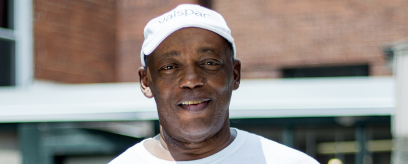 Extreme close-up of a man smiling, wearing a Valspar branded cap and white t-shirt.