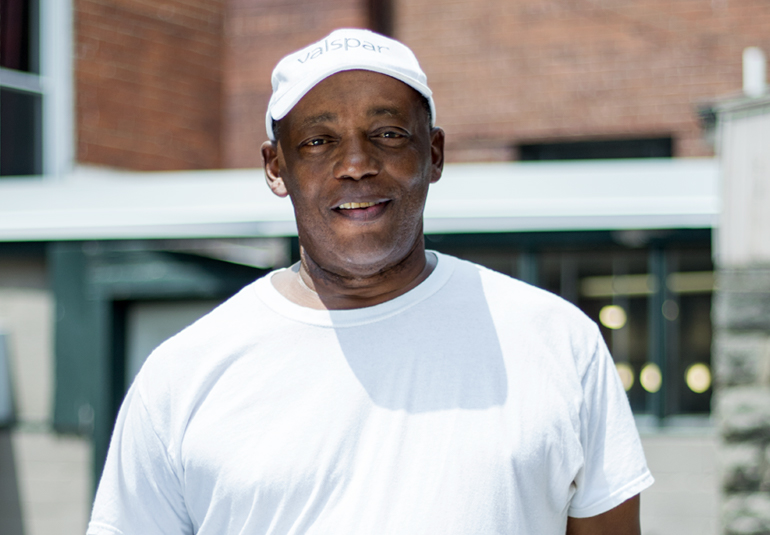 Close-up of a man smiling, wearing a Valspar branded cap and white t-shirt.